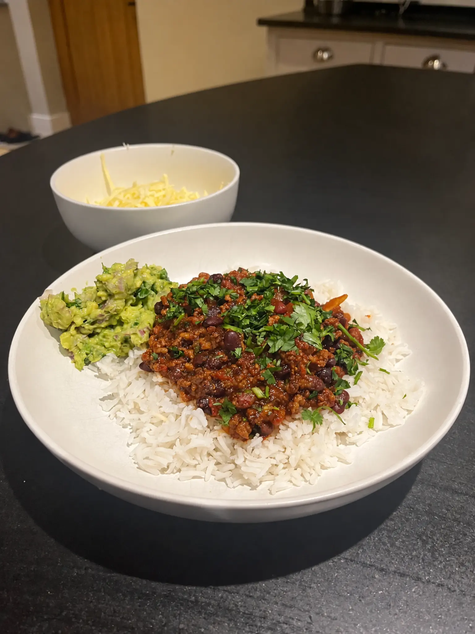 Weeknight beef chilli served over basmati rice with guacamole, coriander and grated Cheddar alongside